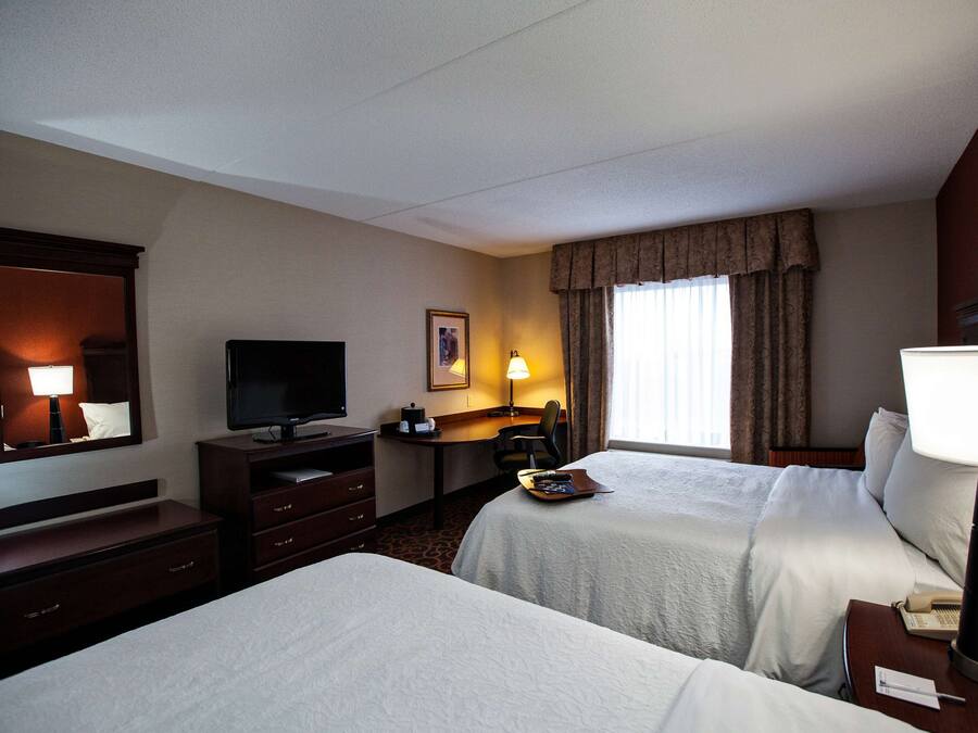 Habitación de hotel con dos camas, un escritorio, un televisor y una ventana con cortinas.