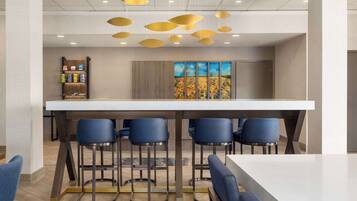 A modern bar area with a white countertop, four blue bar stools, and a hanging light fixture.