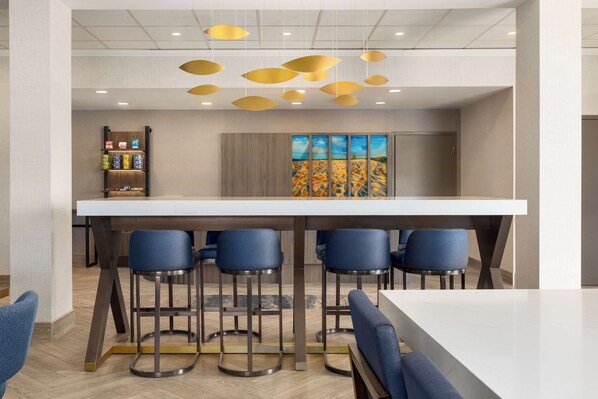 A modern bar area with a white countertop, four blue bar stools, and a hanging light fixture.
