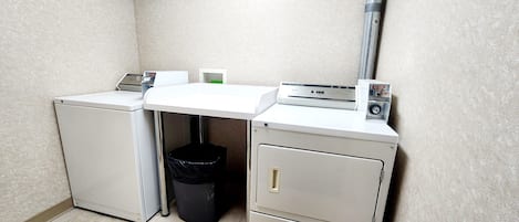 A compact utility room with a washing machine, a small trash bin, and a filing cabinet.