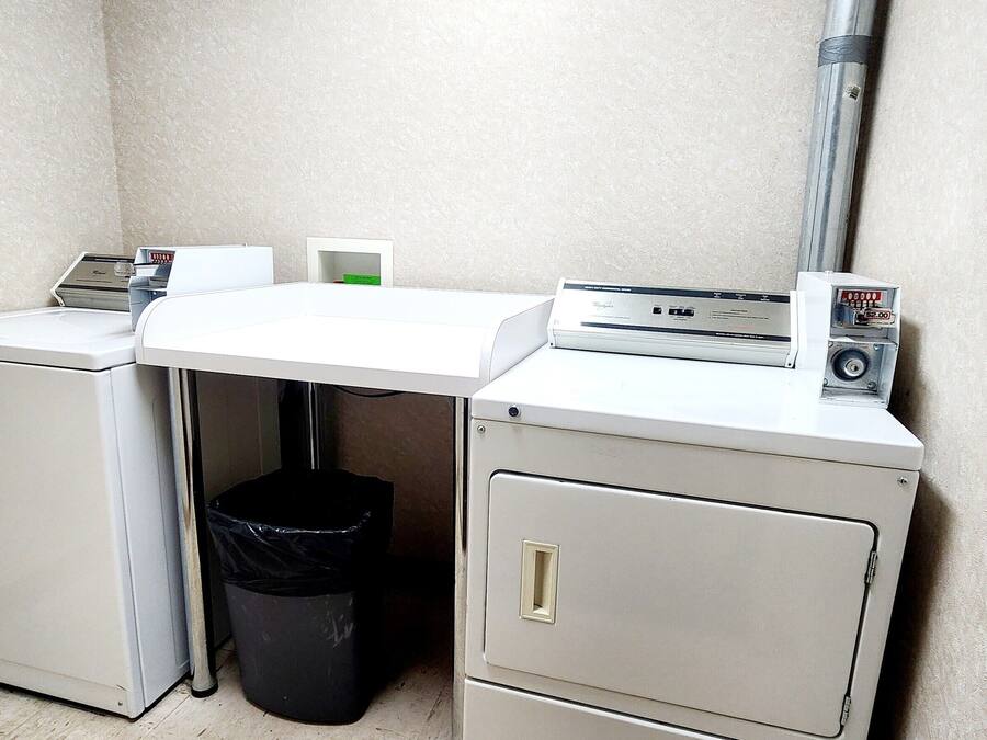 Un cuarto de servicio pequeño y funcional con lavadora, un cubo de basura y un archivador.