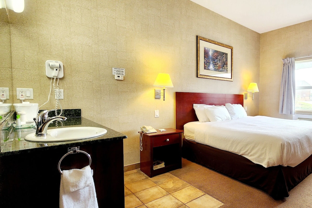 A hotel room with a bed, bedside lamps, a desk with a lamp, a bathroom with a sink and mirror, and a window with curtains.