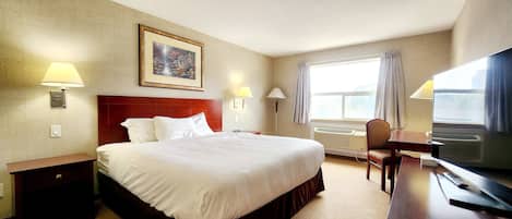 A hotel room with a large bed, two bedside lamps, a desk with a TV, a chair, and a window with curtains.