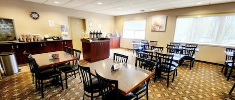 A dining area with tables and chairs, a kitchen counter, and a clock on the wall.