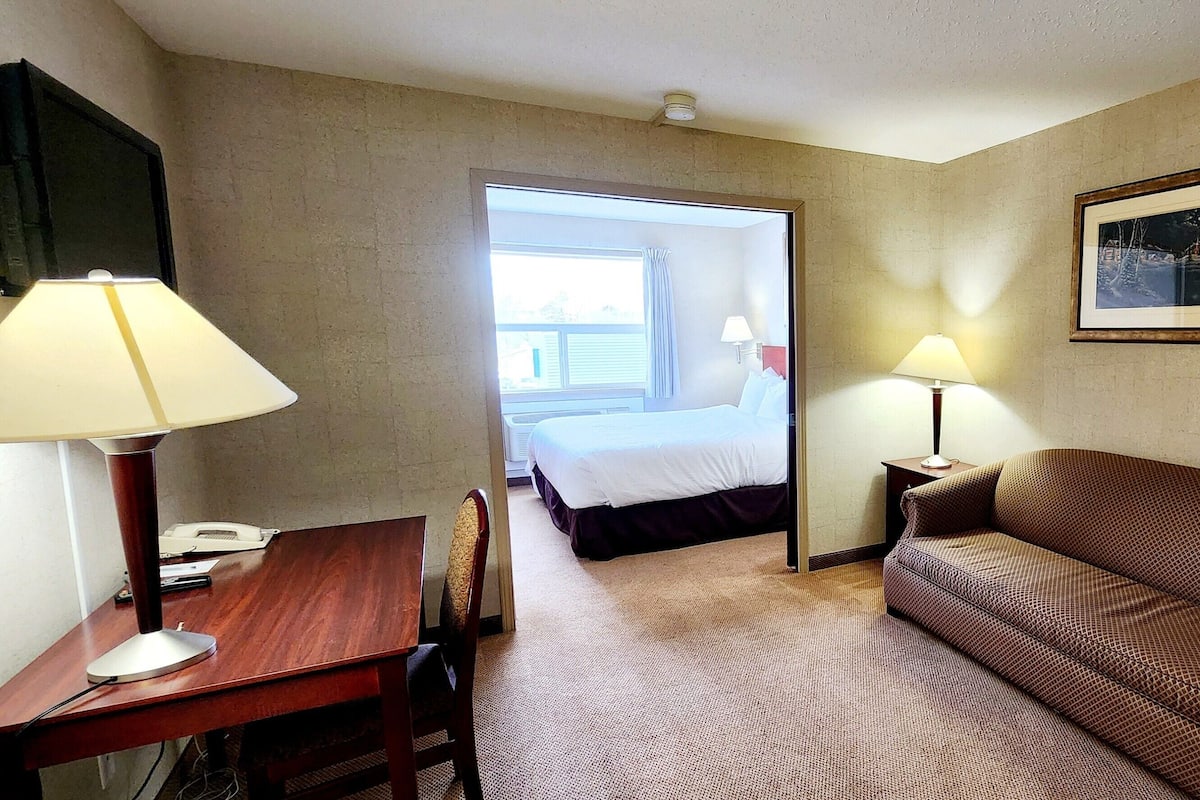 A hotel room with a bed, a desk with a lamp, a sofa, and a framed picture on the wall.