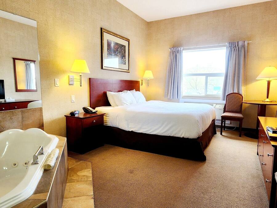 Habitación de hotel con una cama grande, una zona de estar con una silla, un escritorio, un televisor y una bañera.