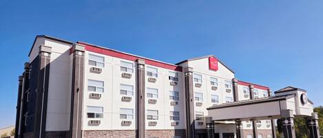 Un hotel de varios pisos con un diseño moderno, que presenta un logo rojo destacado en la fachada.
