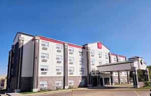 A multi-story hotel with a modern design, featuring a prominent red logo on the facade. - Park Hill Inn & Suites (Red Deer)