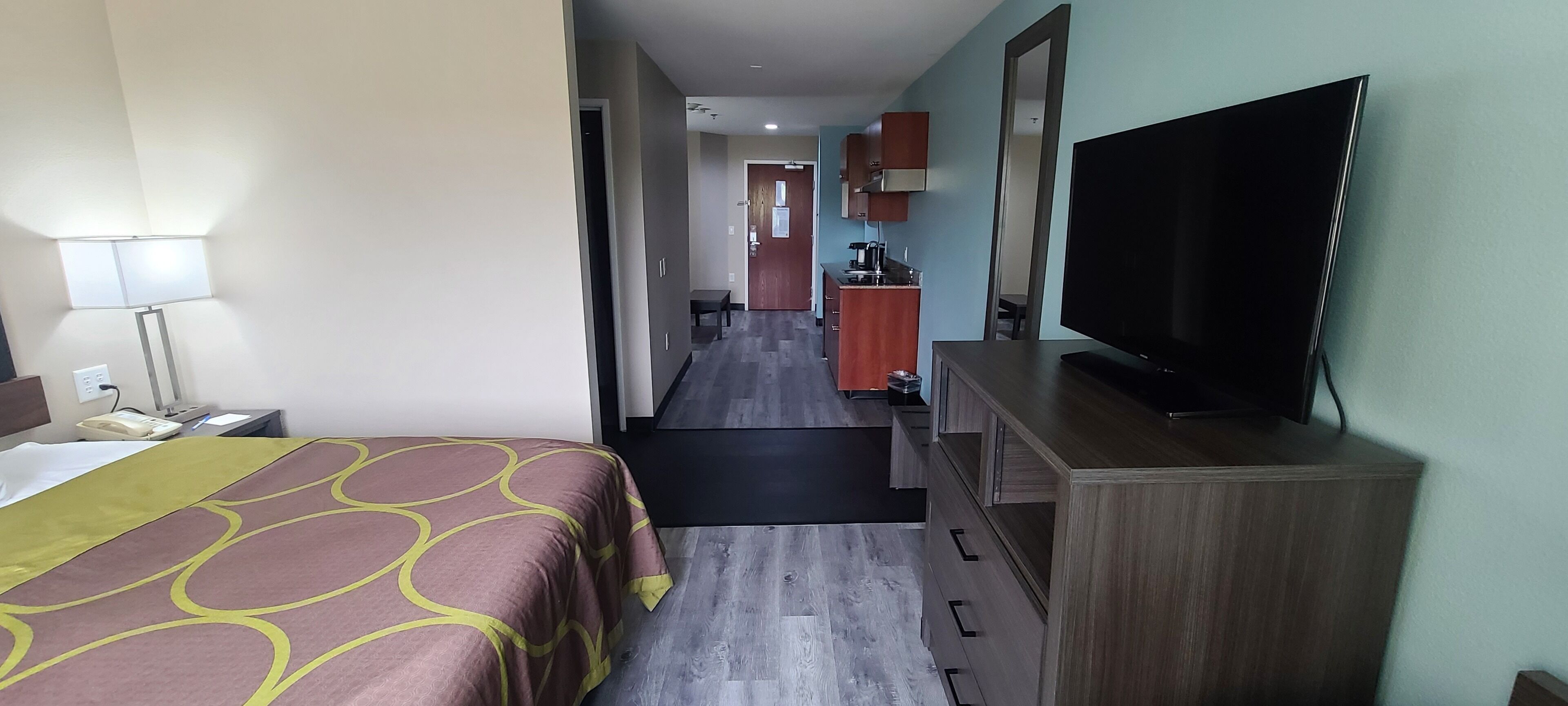 A hotel room with a bed, a TV, a desk, and a kitchenette.