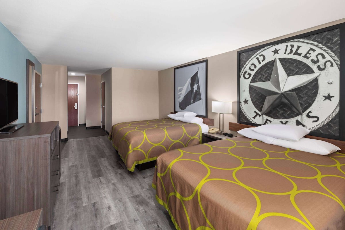 Een hotelkamer met twee bedden, een televisie, een bureau en een muur met een groot embleem.
