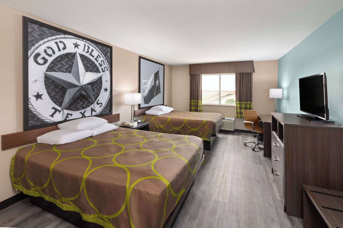 Een hotelkamer met twee bedden, een televisie, een bureau en een raam met gordijnen.