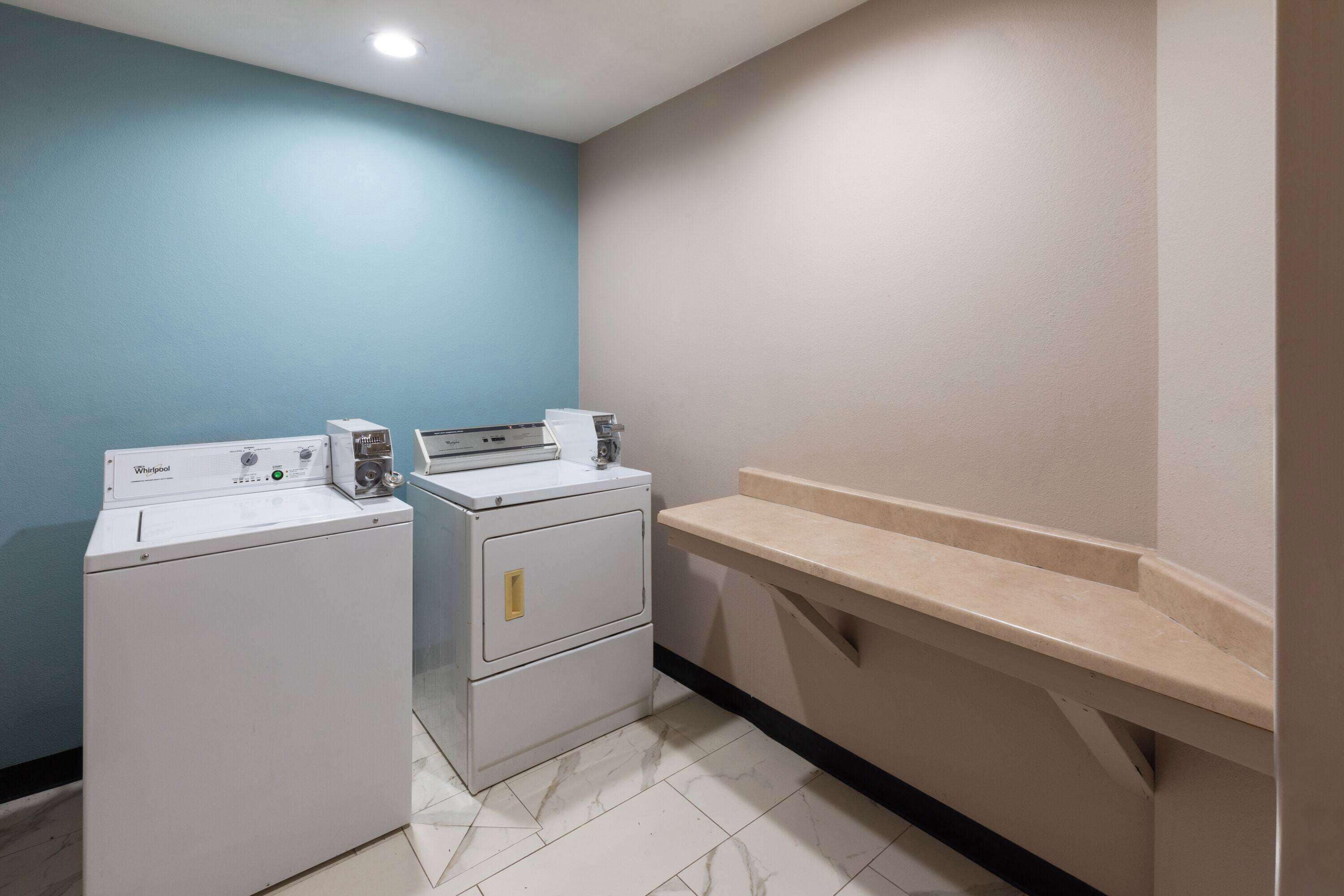 A laundry area with two white Whirlpool washers, a beige countertop, and a blue wall.