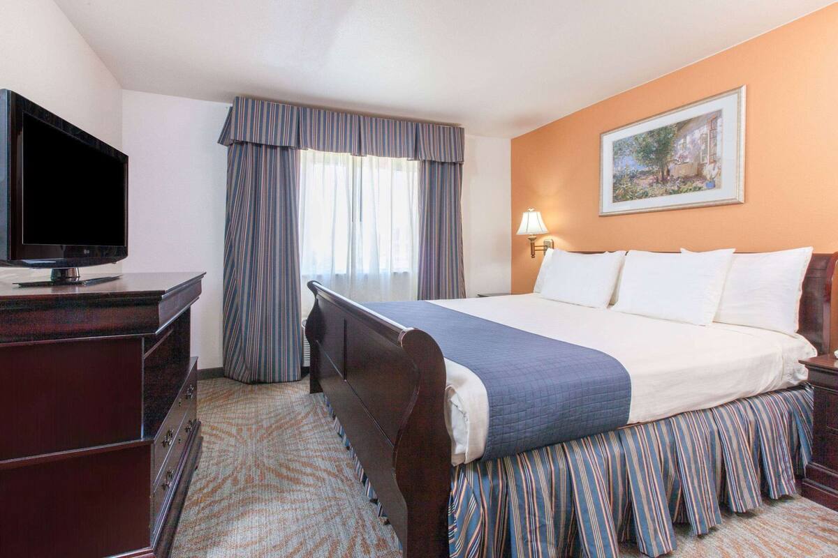 Een hotelkamer met een bed, een bureau met een televisie, een lamp en een schilderij aan de muur.