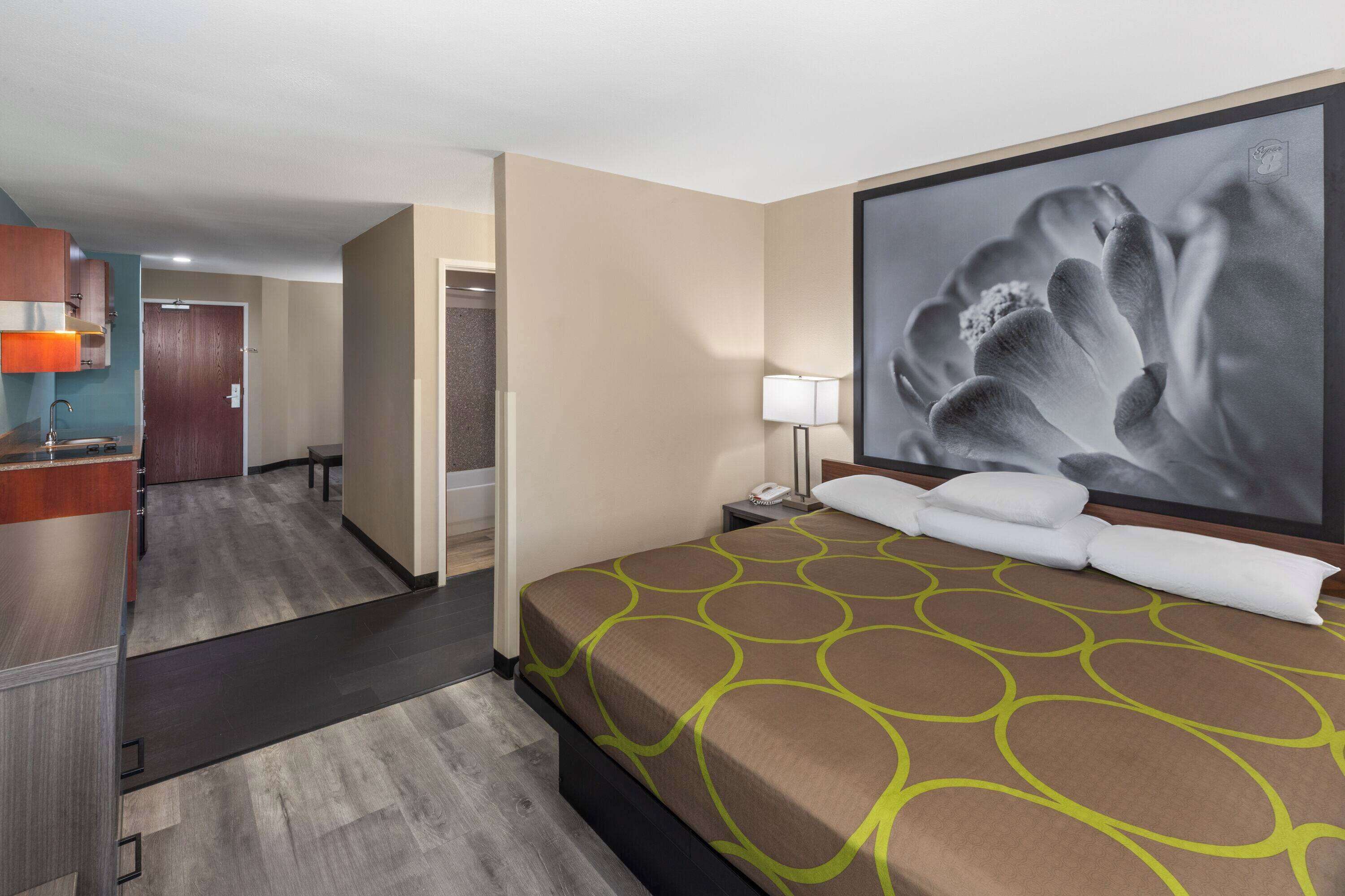 Habitación de hotel con una cama, un escritorio, una silla, una lámpara y un cuadro grande en la pared.