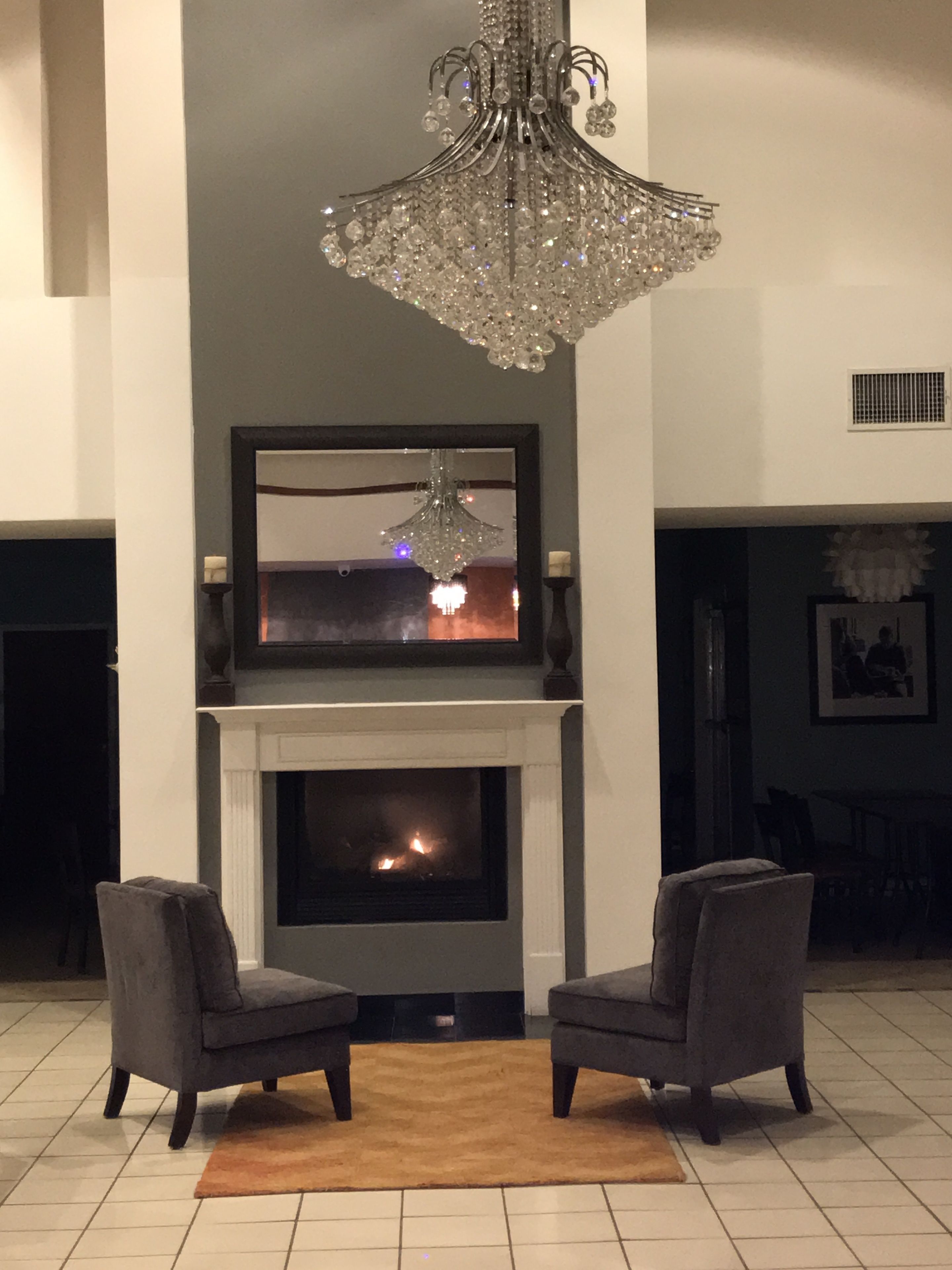Un salon avec une cheminée, deux fauteuils et un lustre.