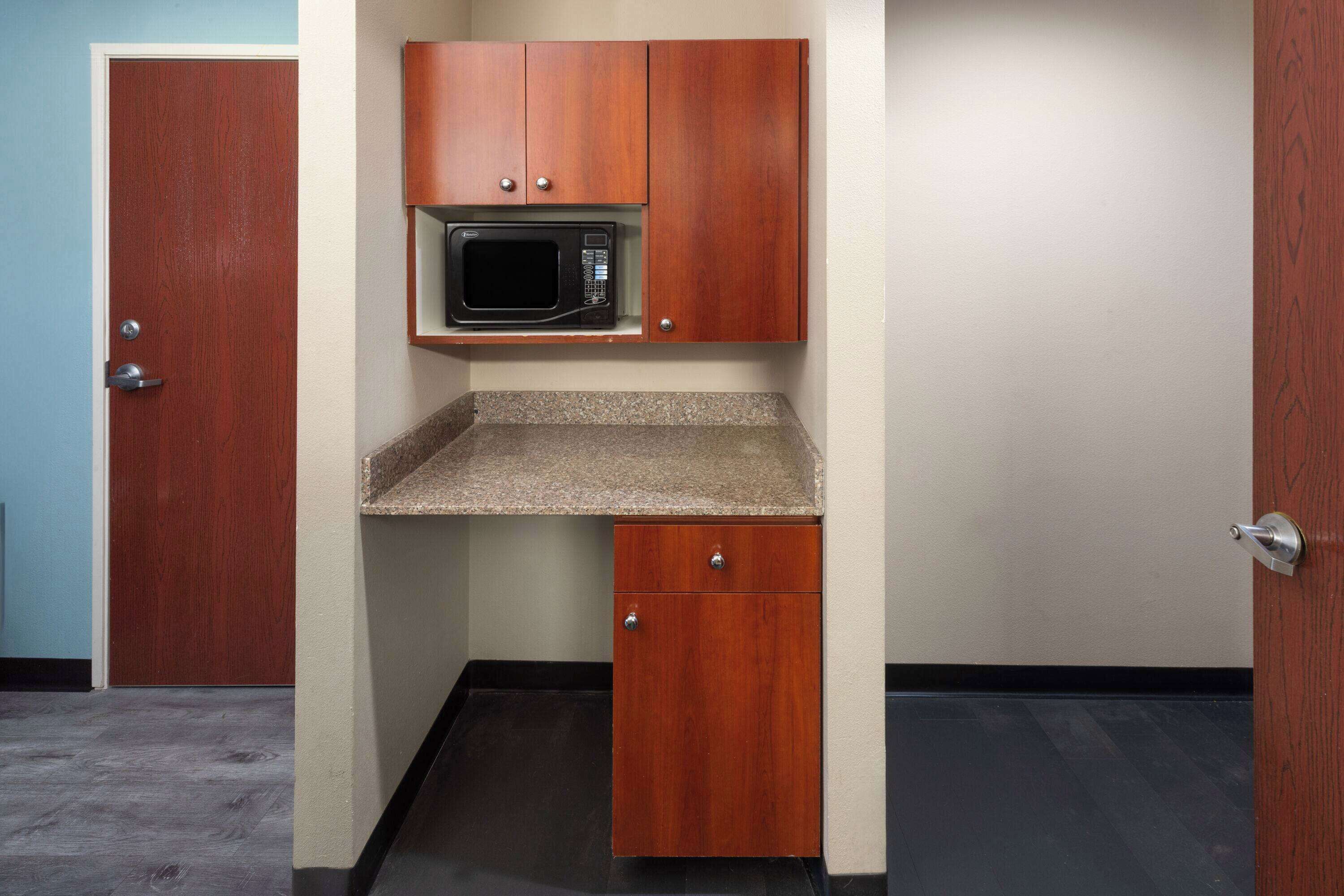 A compact kitchenette with a microwave, a small countertop, and wooden cabinets.