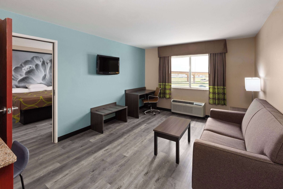 Een hotelkamer met een bed, bureau, stoel, bank, televisie en een raam met gordijnen.