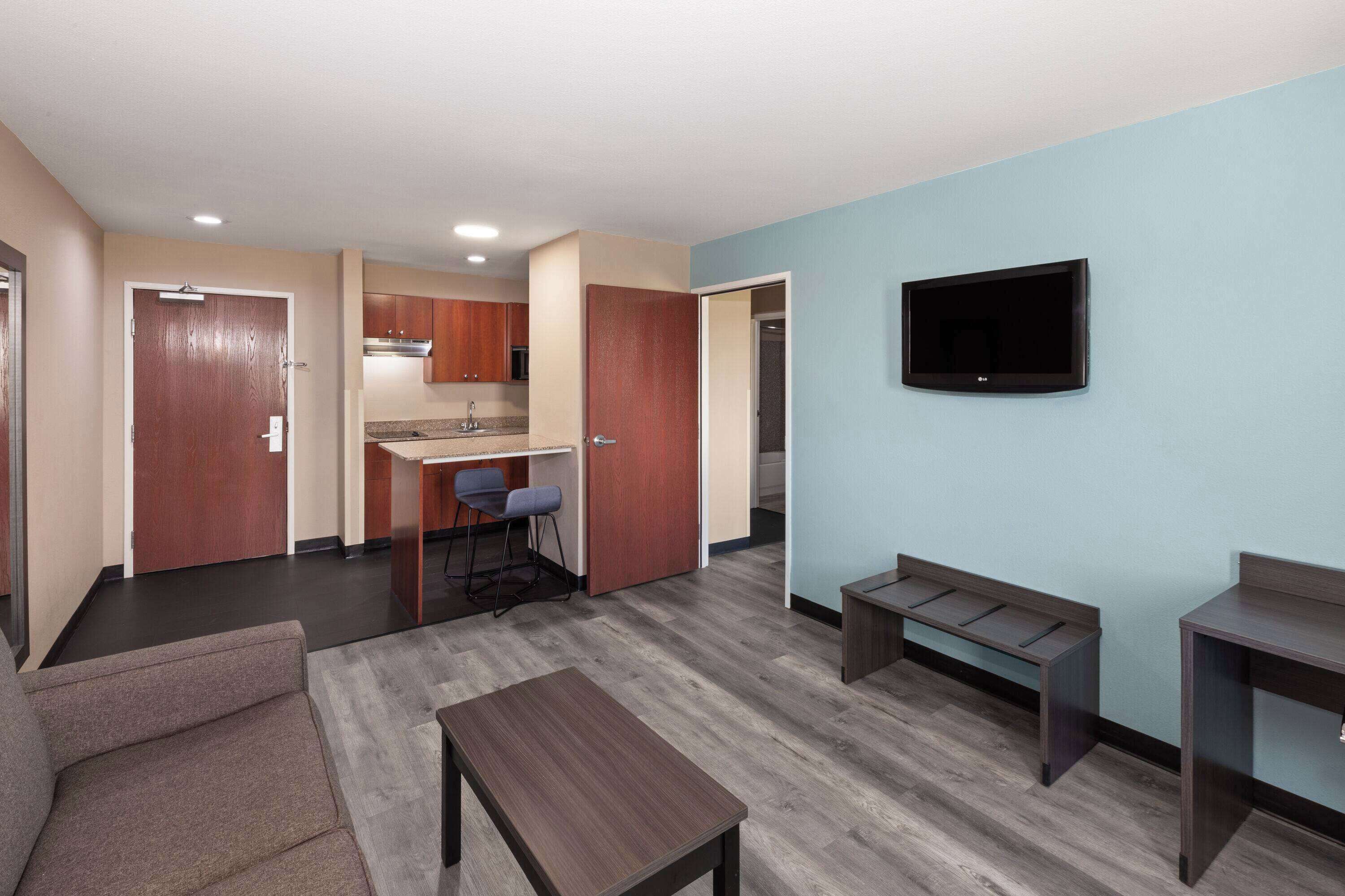 Een modern appartement met een kitchenette, een eethoek, een woonkamer met een bank en een salontafel, en een aan de muur bevestigde televisie.