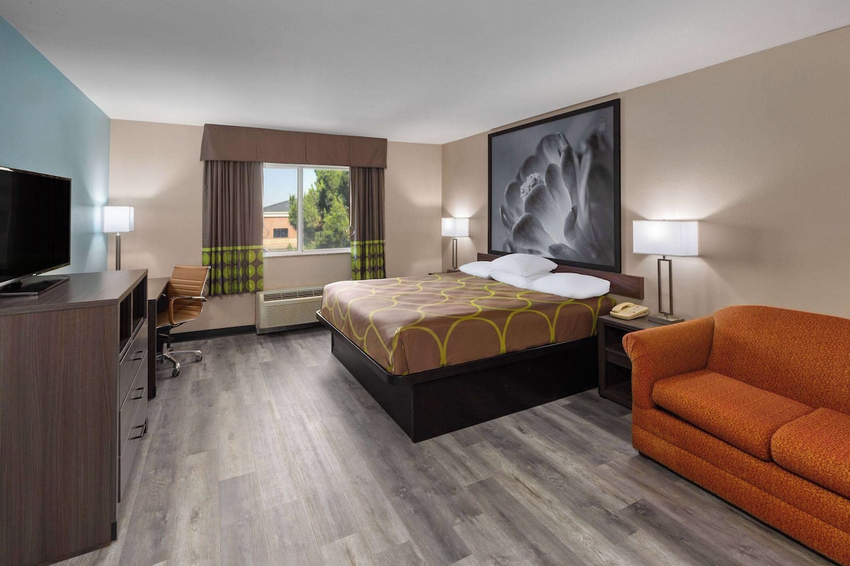Een hotelkamer met een bed, televisie, bureau, stoel, bank en een groot raam met gordijnen.