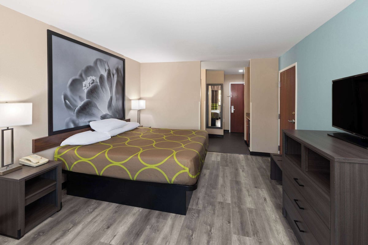 Een hotelkamer met een groot bed, een televisie, een bureau met een lamp en een schilderij aan de muur.