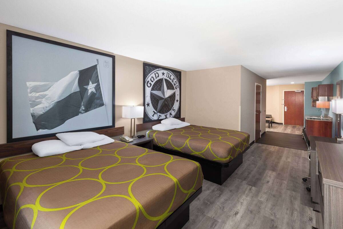 Een hotelkamer met twee bedden, een bureau, een stoel, een badkamer en een gang naar een andere kamer.