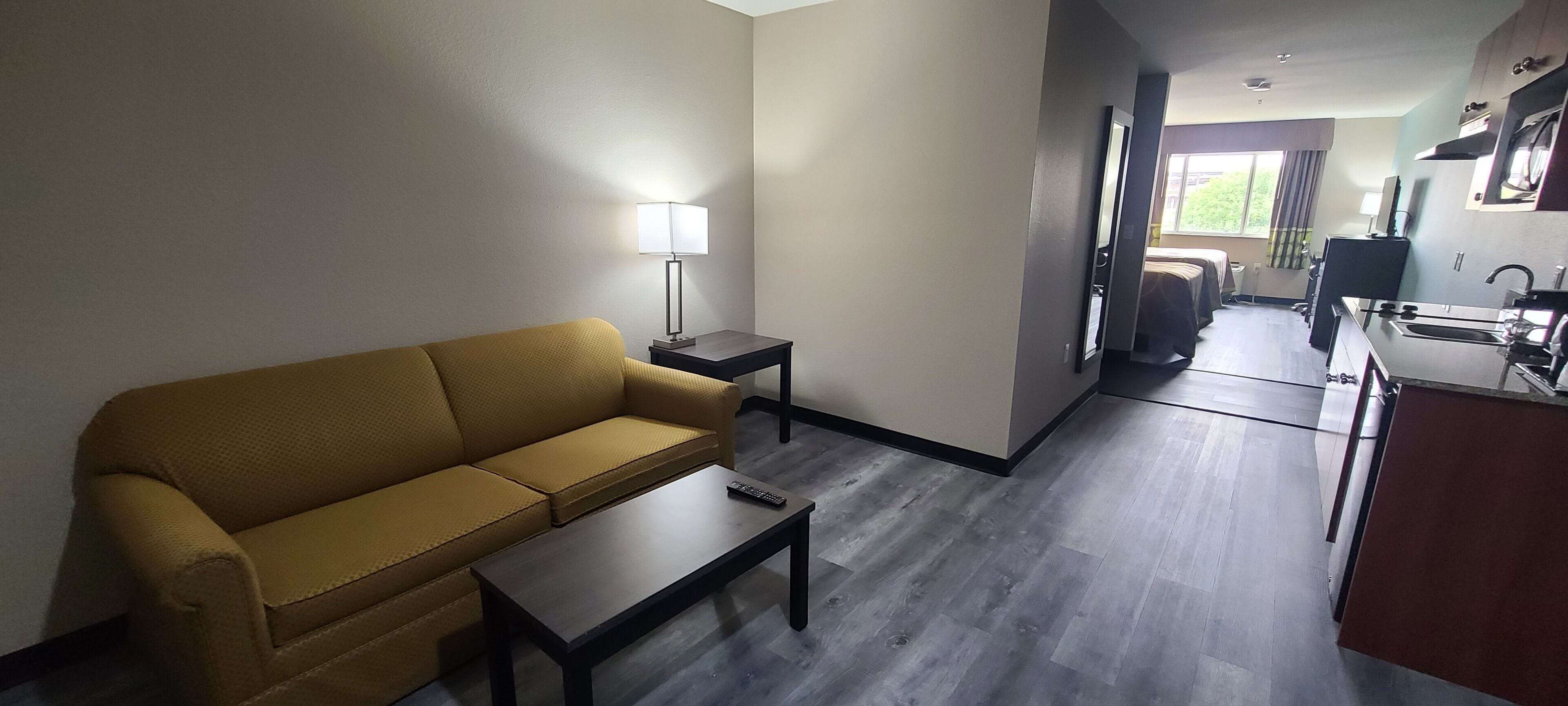 Una habitación de hotel moderna con sofá, una mesita, lámpara y kitchenette.