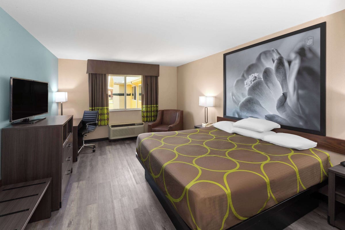 Een hotelkamer met een groot bed, een bureau met een televisie, een stoel en een raam met gordijnen.