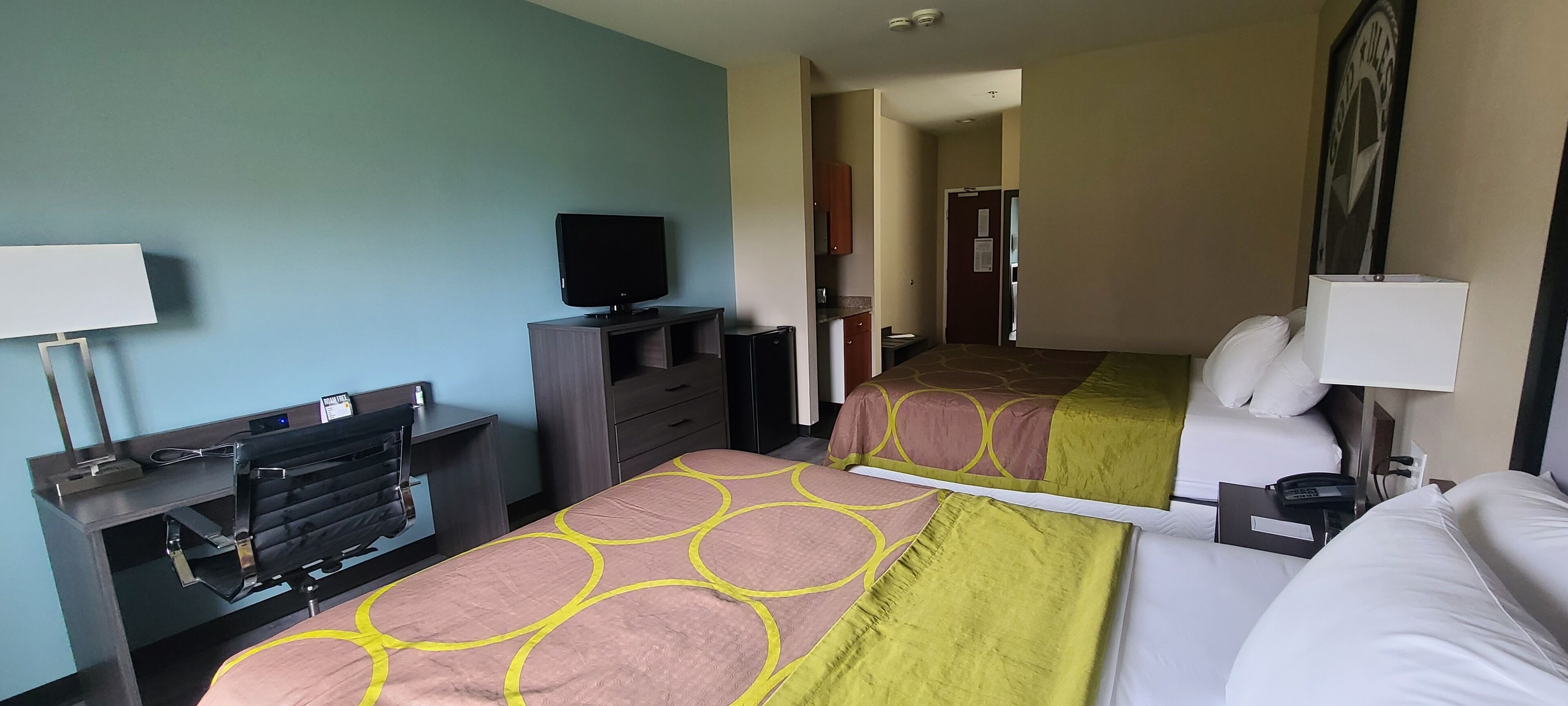 A hotel room with two beds, a television, a desk with a lamp, and a door leading to a hallway.