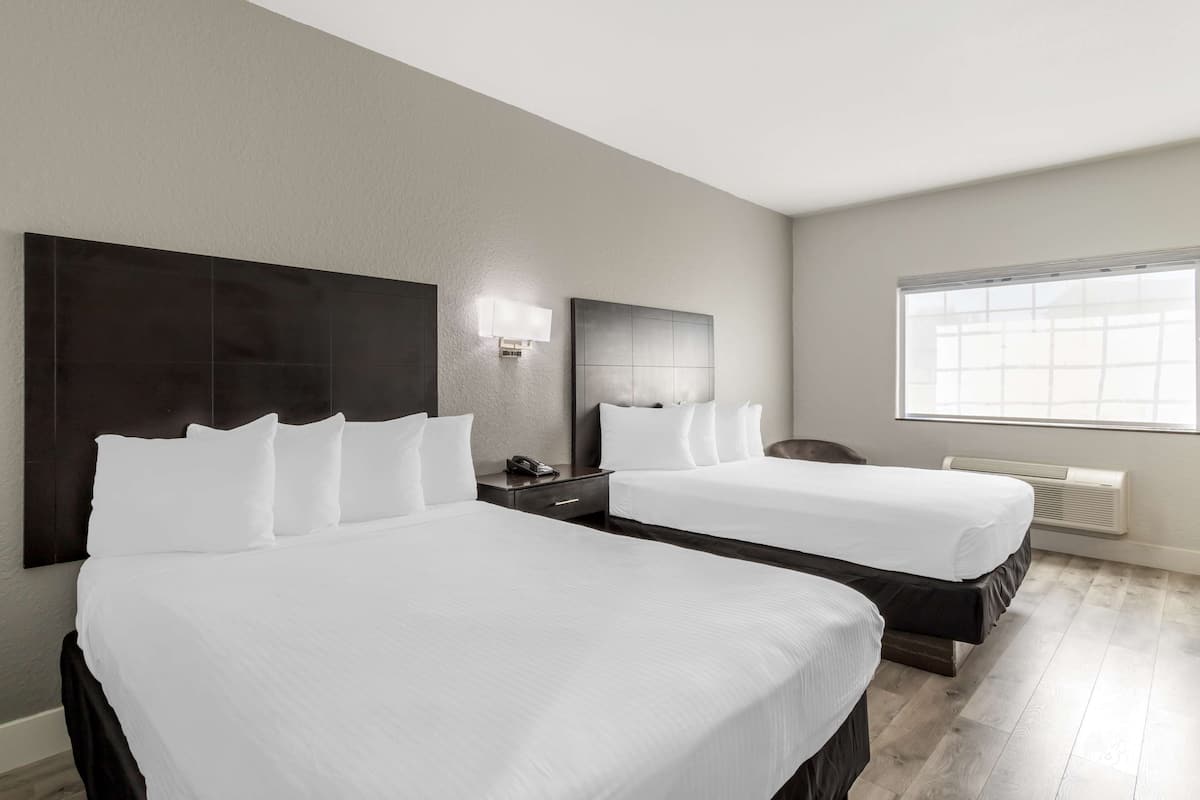 Ein Hotelzimmer mit zwei Betten, einem Nachttisch, einem Schreibtisch, einem Sessel und einem großen Fenster.