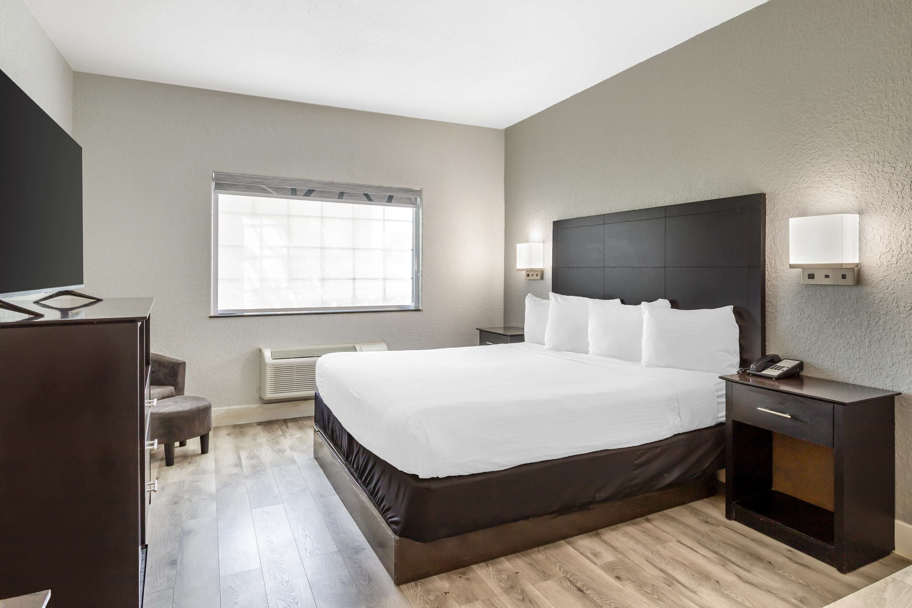 Une chambre d’hôtel moderne avec un grand lit, des tables de chevet, un bureau et une fenêtre équipée de stores.