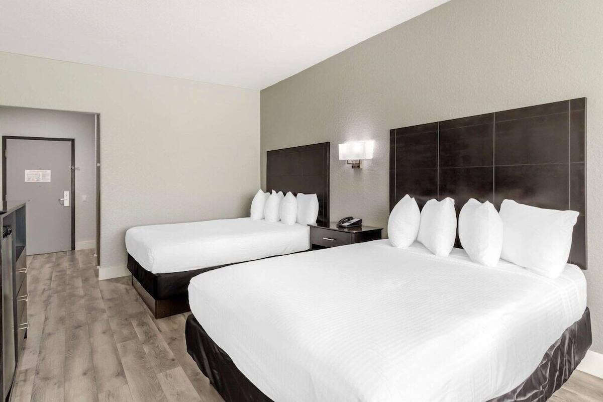 Ein Hotelzimmer mit zwei Betten, einem Schreibtisch, einem Stuhl, einem Fernseher und einer Tür.