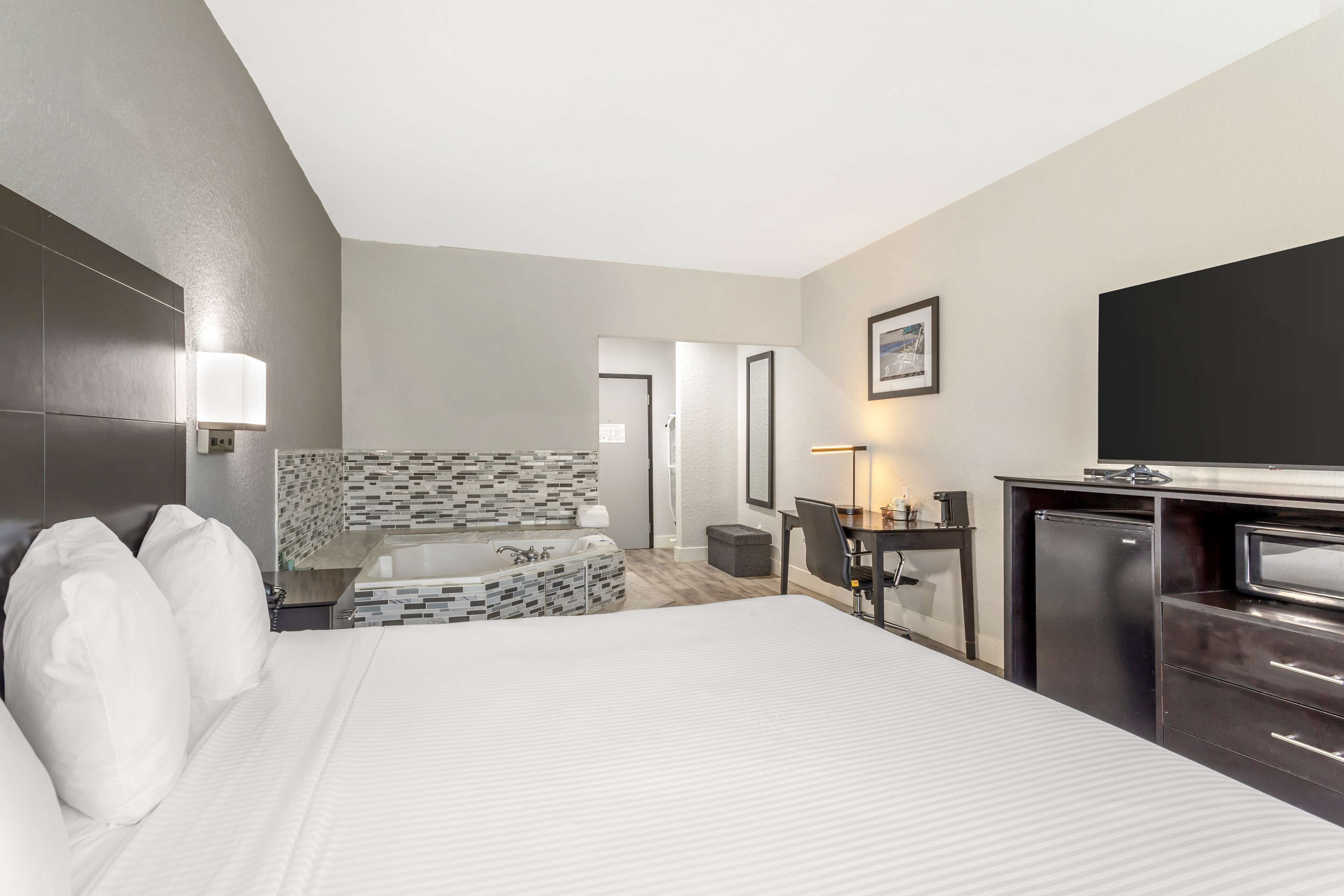 Habitación de hotel con una cama grande, un escritorio con televisor de pantalla plana, una pequeña kitchenette y un baño con ducha azulejada.