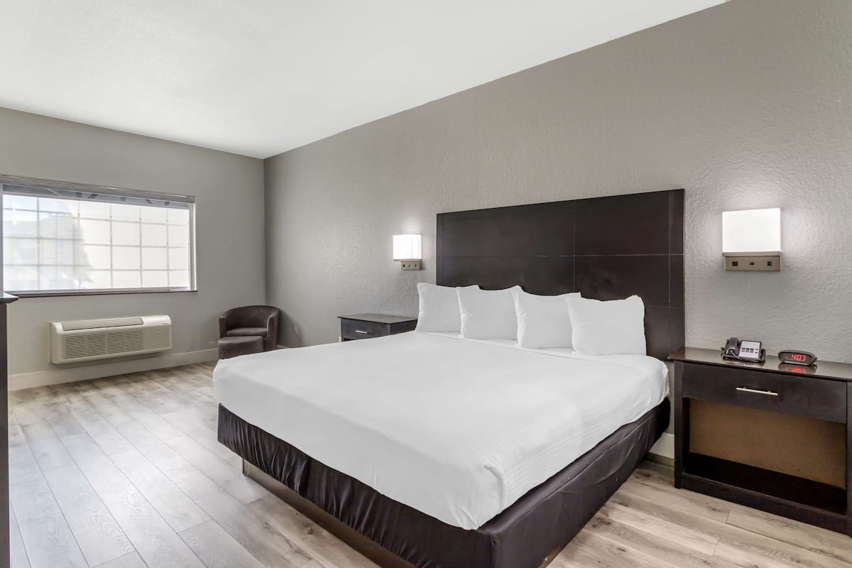 Ein modernes Hotelzimmer mit einem großen Bett, Nachttischen, einem Sessel und einem Fenster.