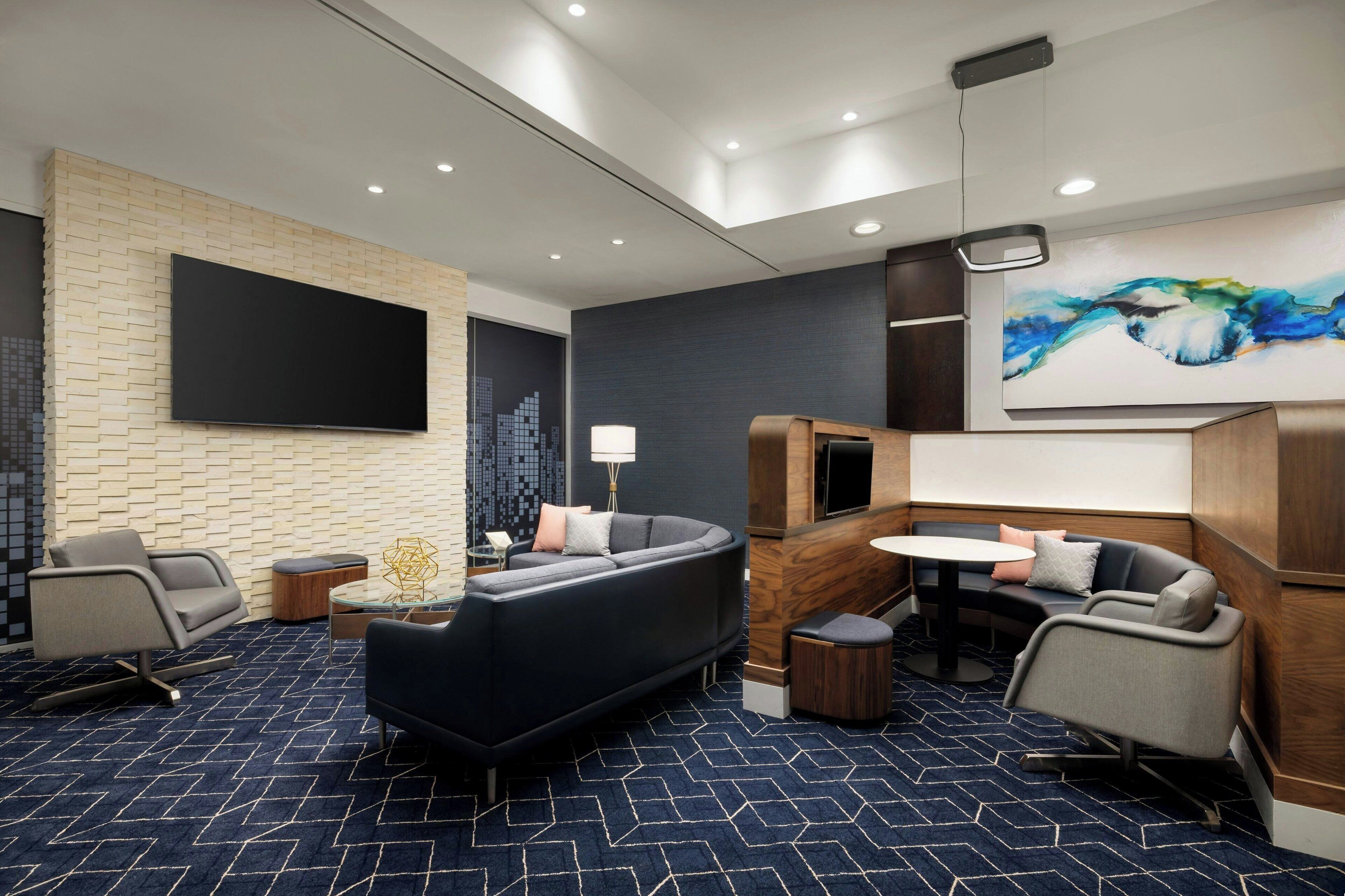 A modern hotel room with a large flat-screen TV, a sofa, a small round table, and a painting on the wall.