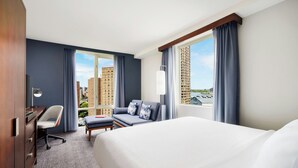 Habitación de hotel con una cama grande, un escritorio con silla, un sofá y vistas a edificios altos.