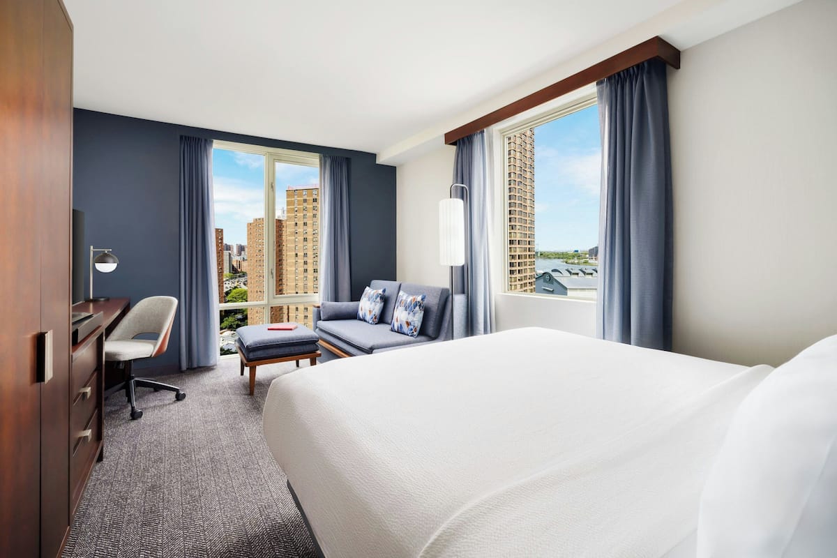Habitación de hotel con una cama grande, un escritorio con silla, un sofá y vistas a edificios altos.
