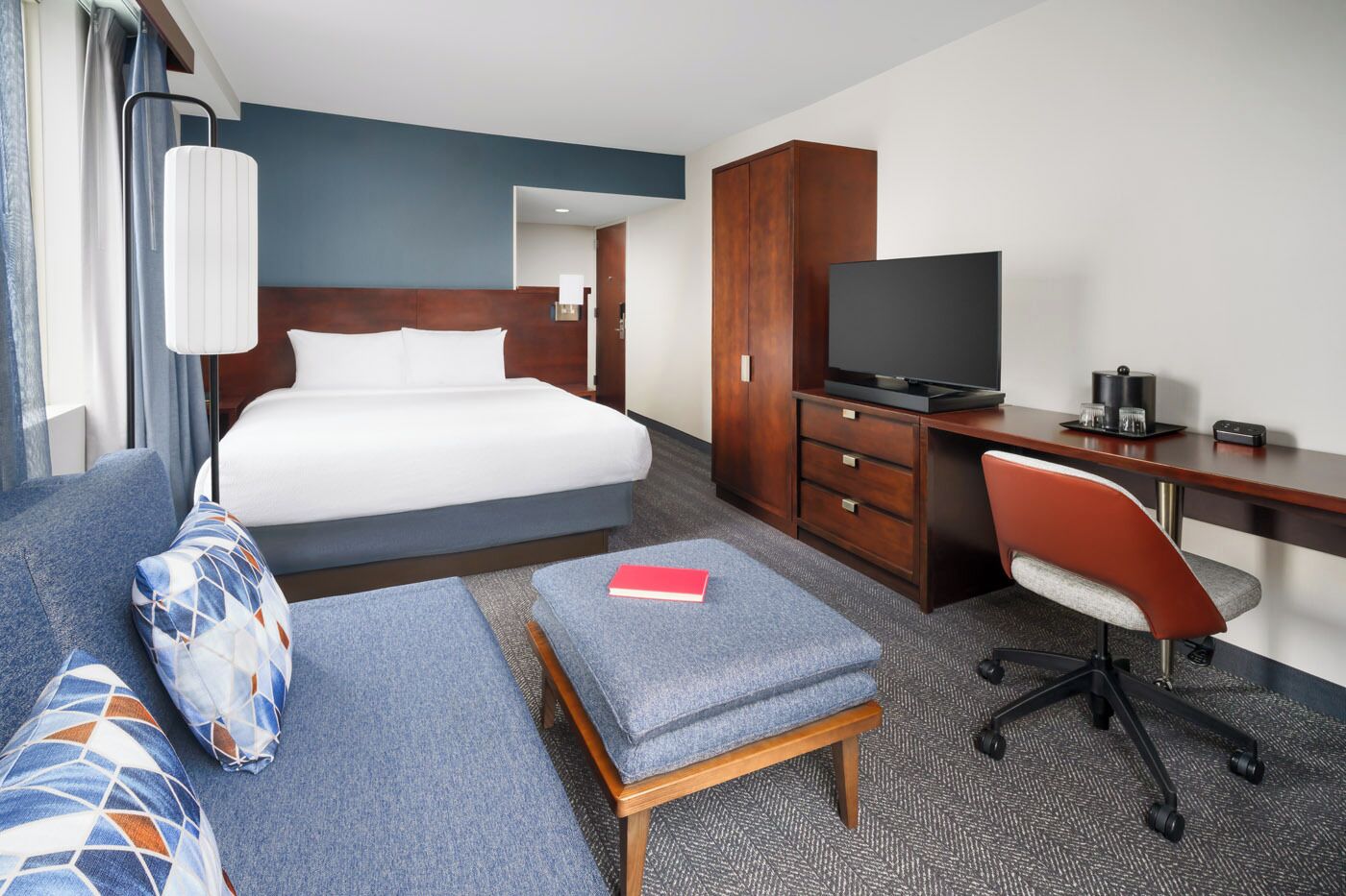 A hotel room with a bed, a desk, a TV, a chair, and a sofa.