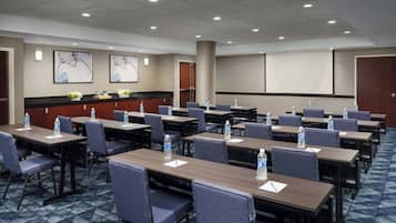 A conference room with multiple tables and chairs, equipped with water bottles and notepads.
