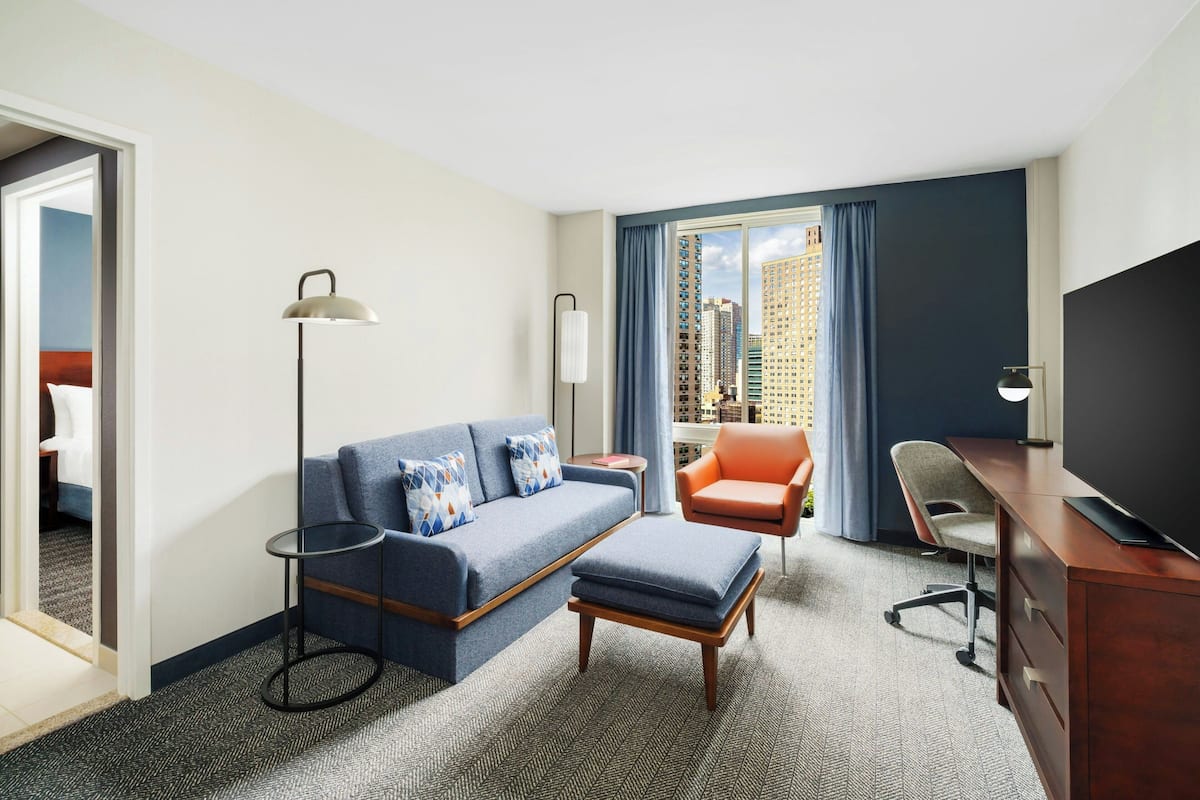 Habitación de hotel con sofá, sillón, escritorio y televisor.