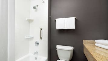 A modern bathroom with a white bathtub, a shower, a toilet, and a granite countertop.