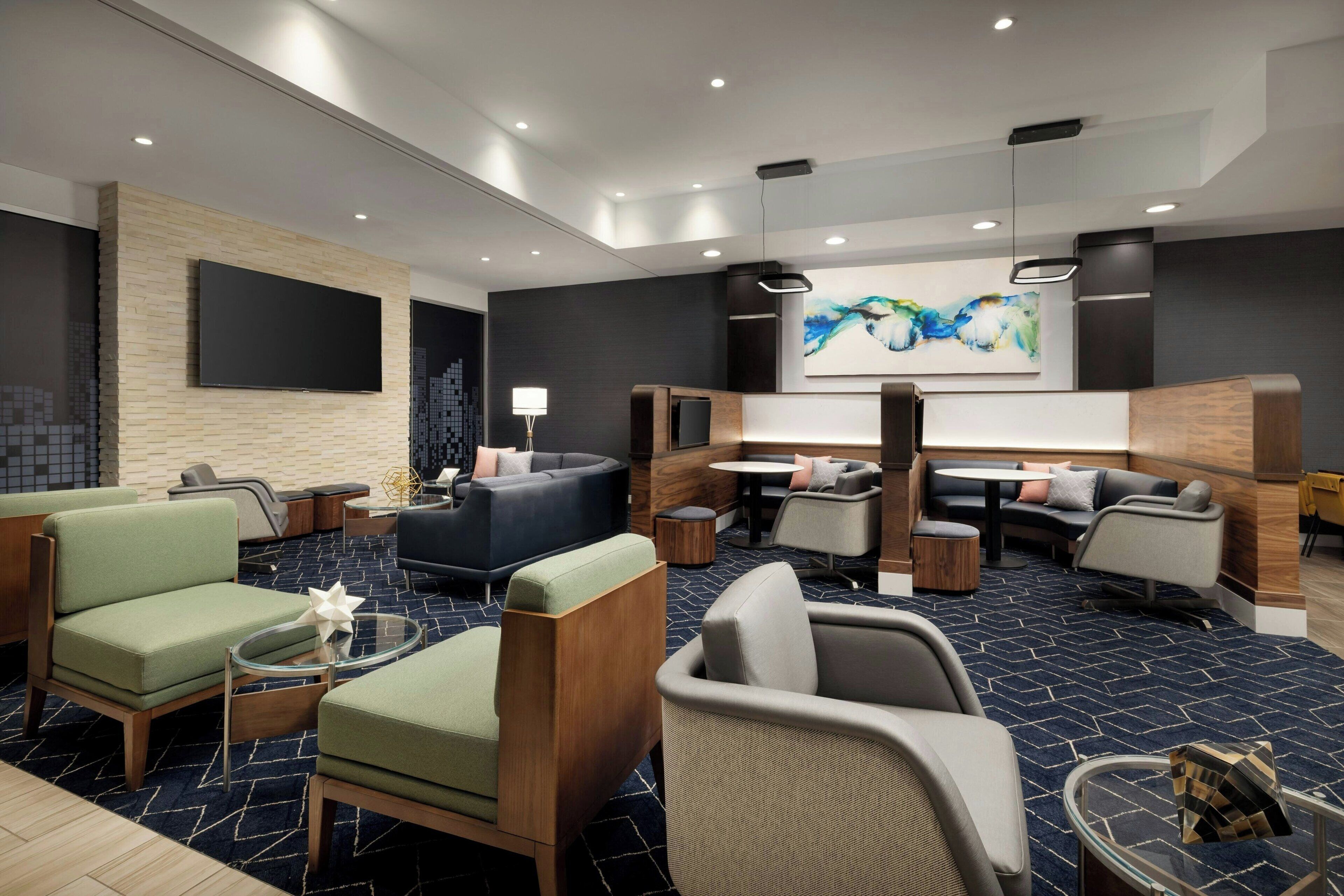 Eine moderne Hotellobby mit einem großen Fernseher, gemütlichen Sitzbereichen und einem großen abstrakten Gemälde an der Wand.