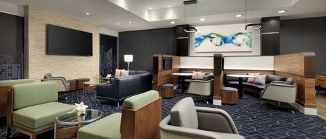 A modern hotel lobby with a large TV, comfortable seating areas, and a large abstract painting on the wall.
