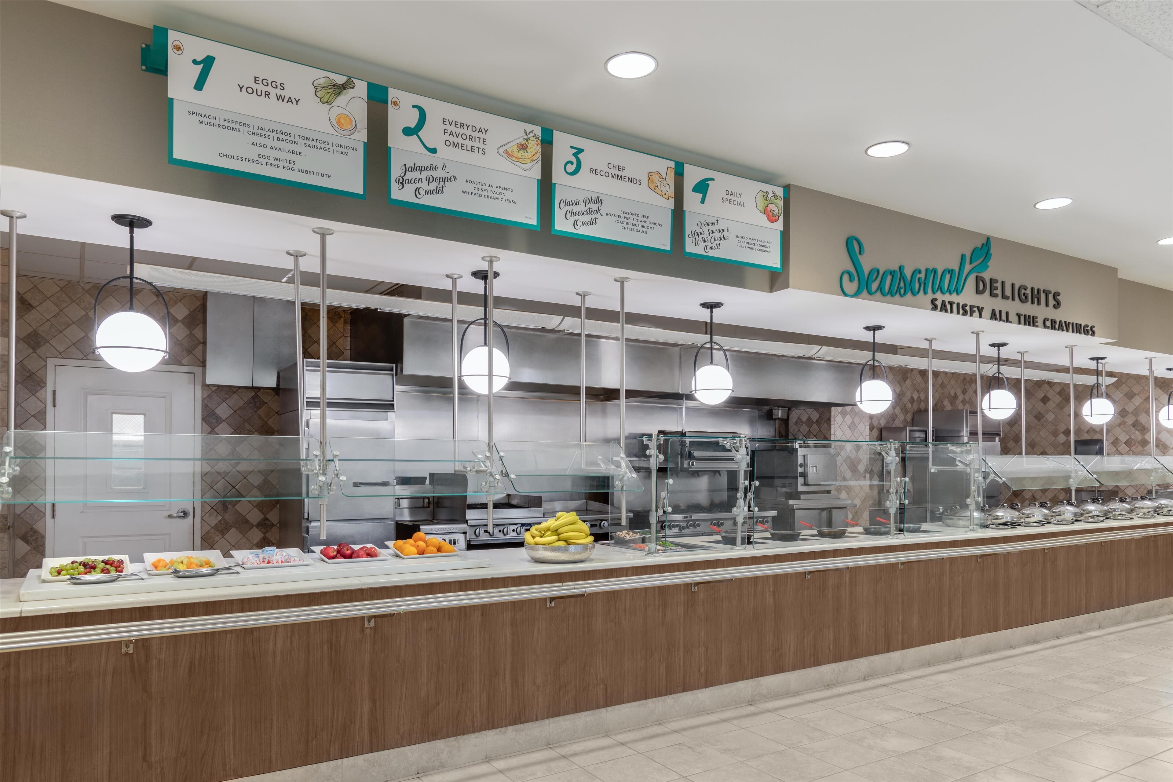 Zona de bufé con señalización clara para las opciones de comida, incluyendo huevos, deliciosos omelettes y sugerencias de quesos.