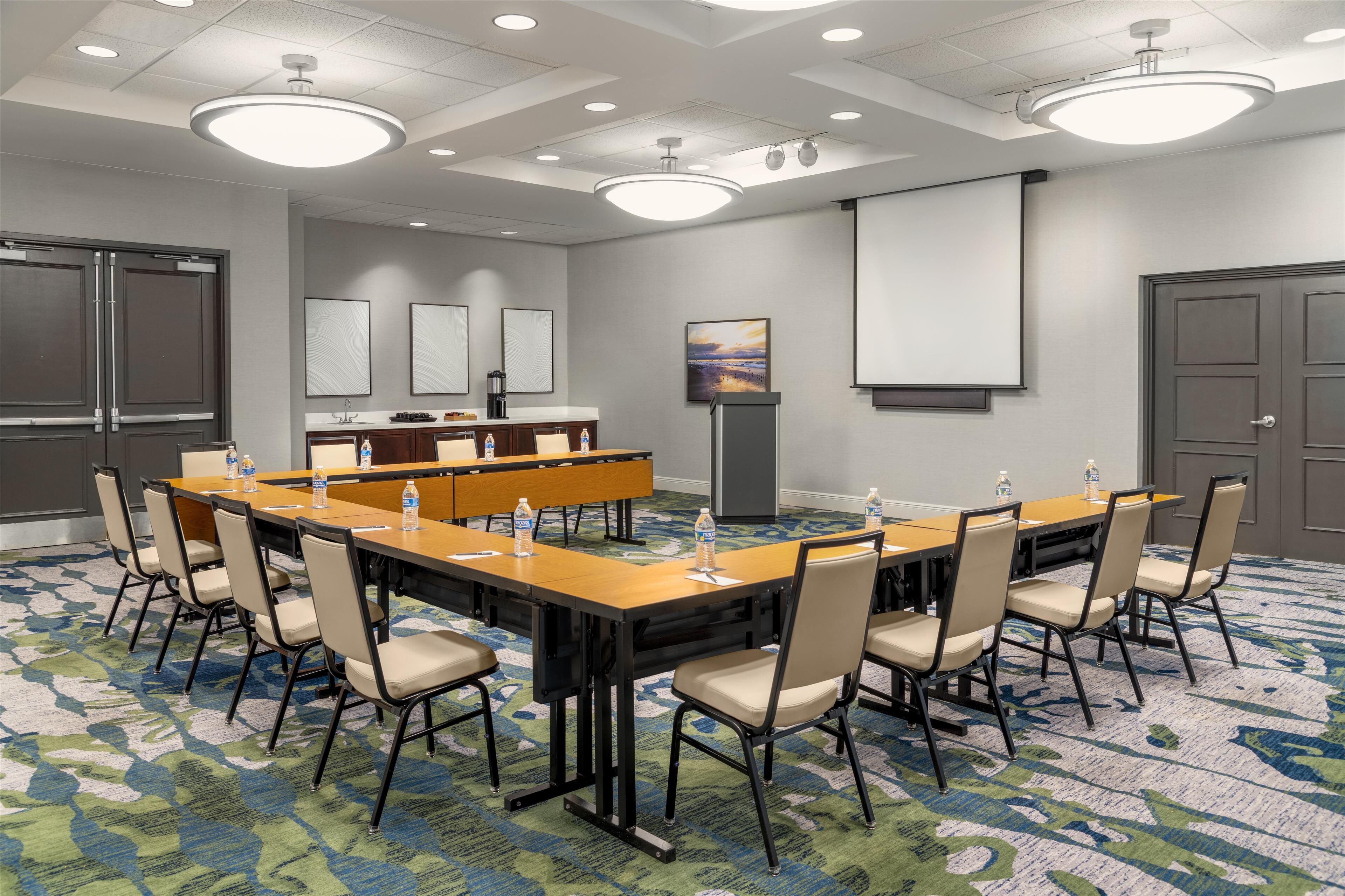 A conference room with a long table, chairs, a projector screen, and a coffee machine.