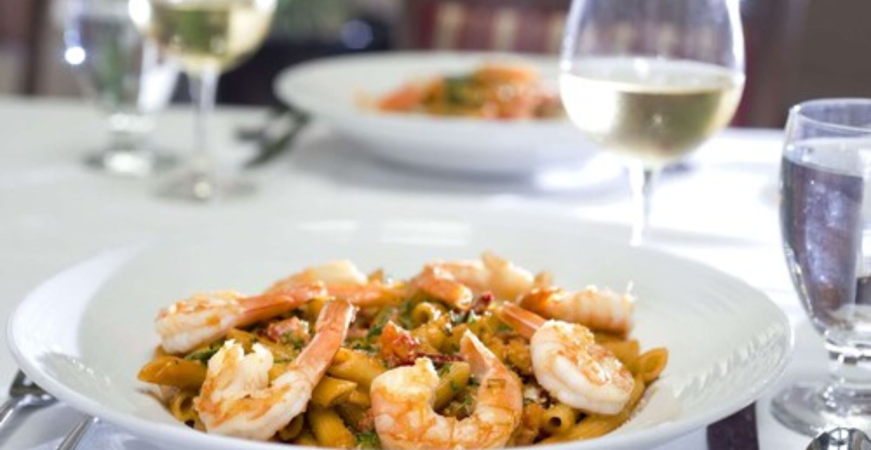A plate of shrimp pasta with a glass of white wine in the background.