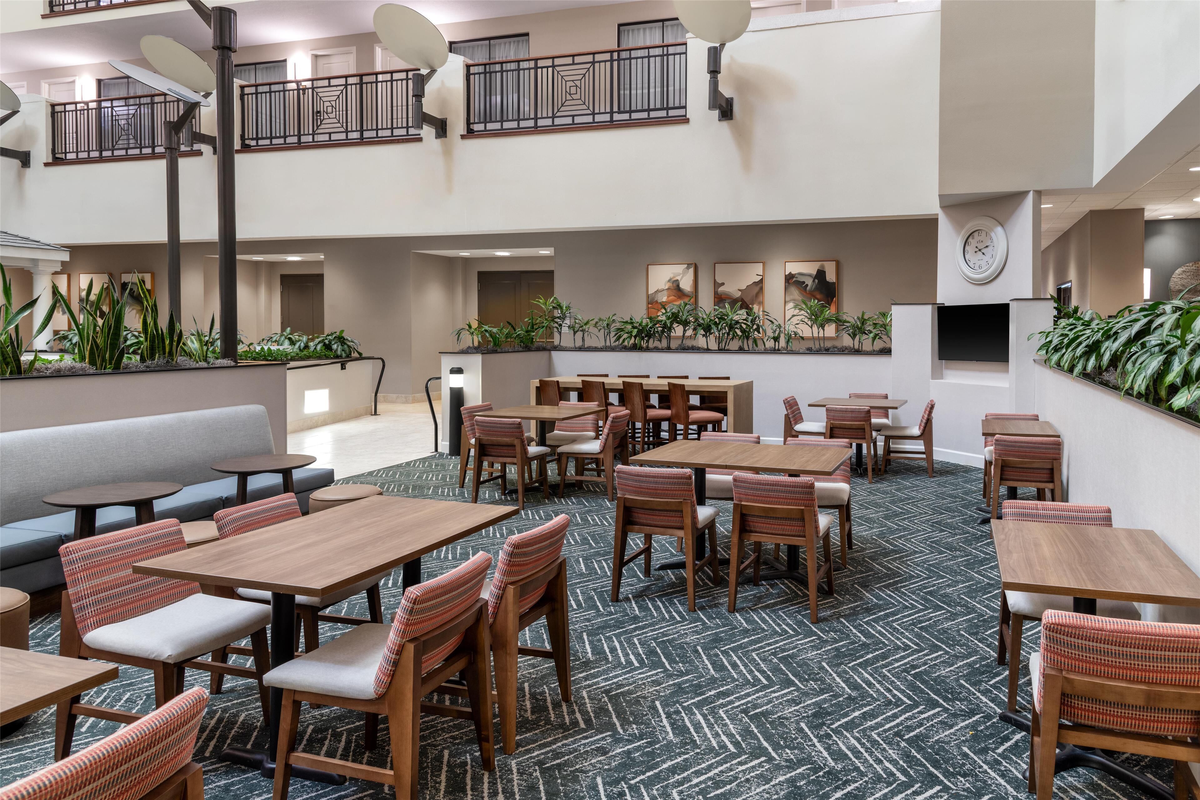 A spacious indoor dining area with multiple tables and chairs, a sofa, and a balcony with plants.