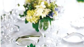 A table set with white plates, silverware, and clear glasses, accompanied by a floral centerpiece.
