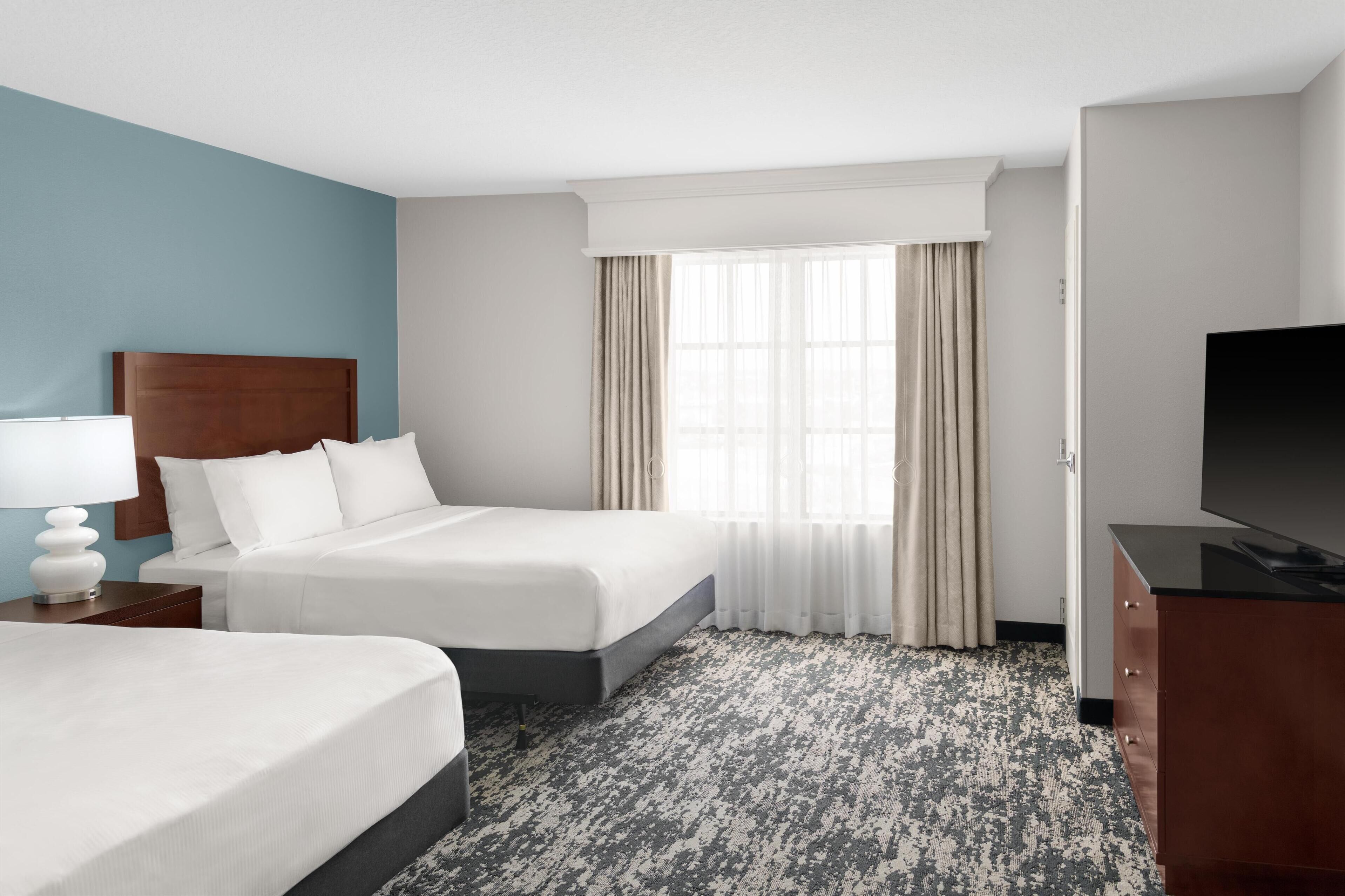 A hotel room with two beds, a TV, a nightstand, and a window with curtains.