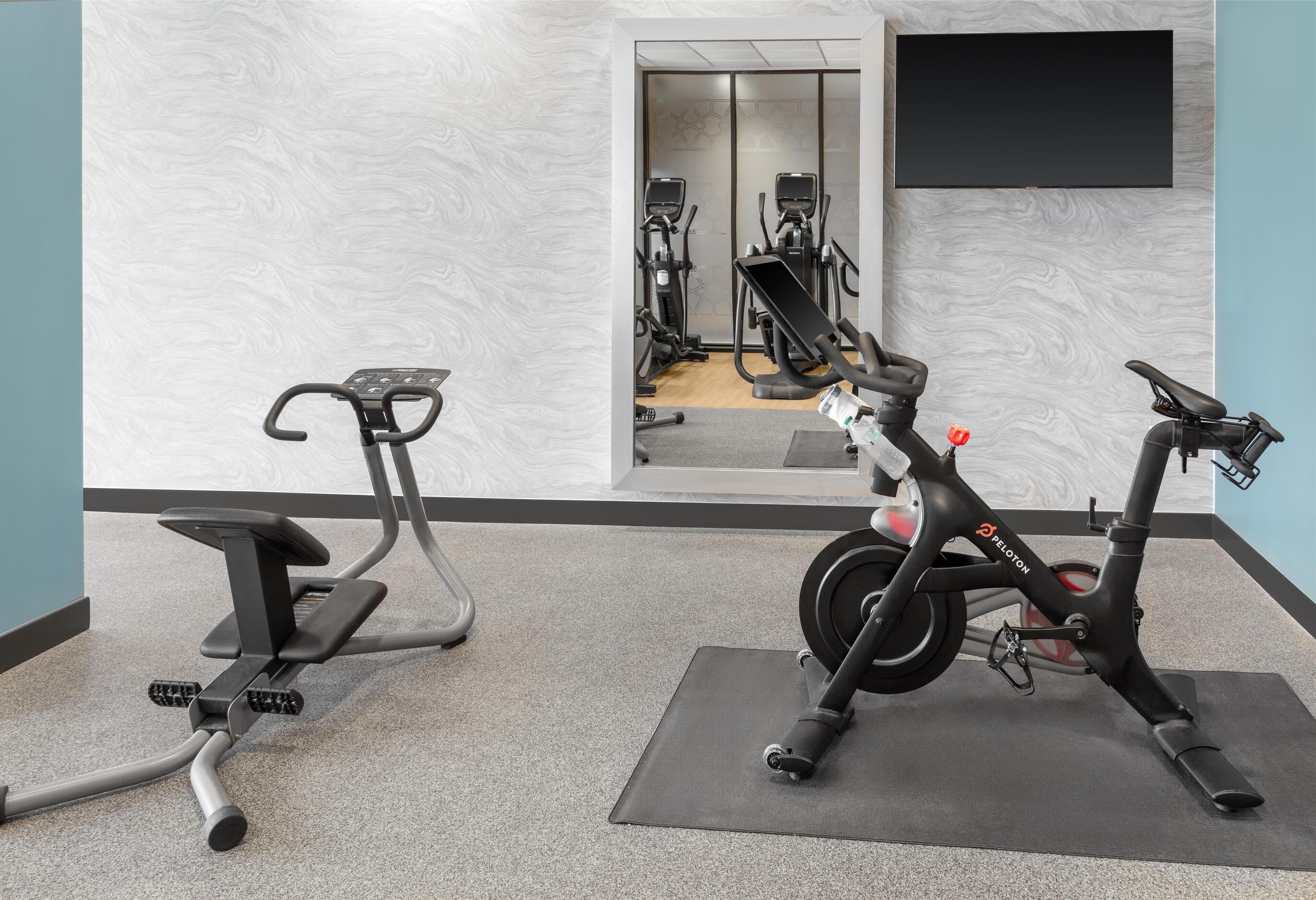 An indoor gym with exercise equipment, including a stationary bike and an elliptical machine, on a carpeted floor.