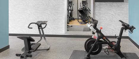 An indoor gym with exercise equipment, including a stationary bike and an elliptical machine, on a carpeted floor.